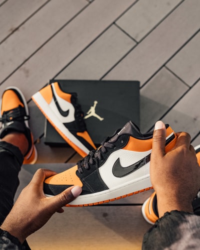 人坐着白色,橙色和黑色的空气约旦1 low-top运动鞋
